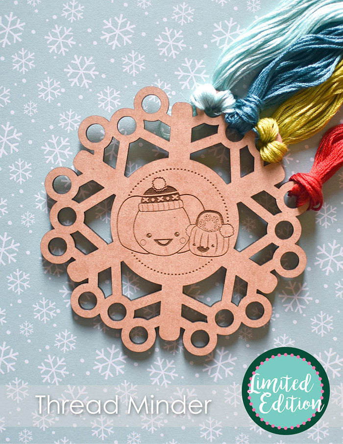 Wooden thread minder in the shape of a snowflake with two pumpkins in snow hats.